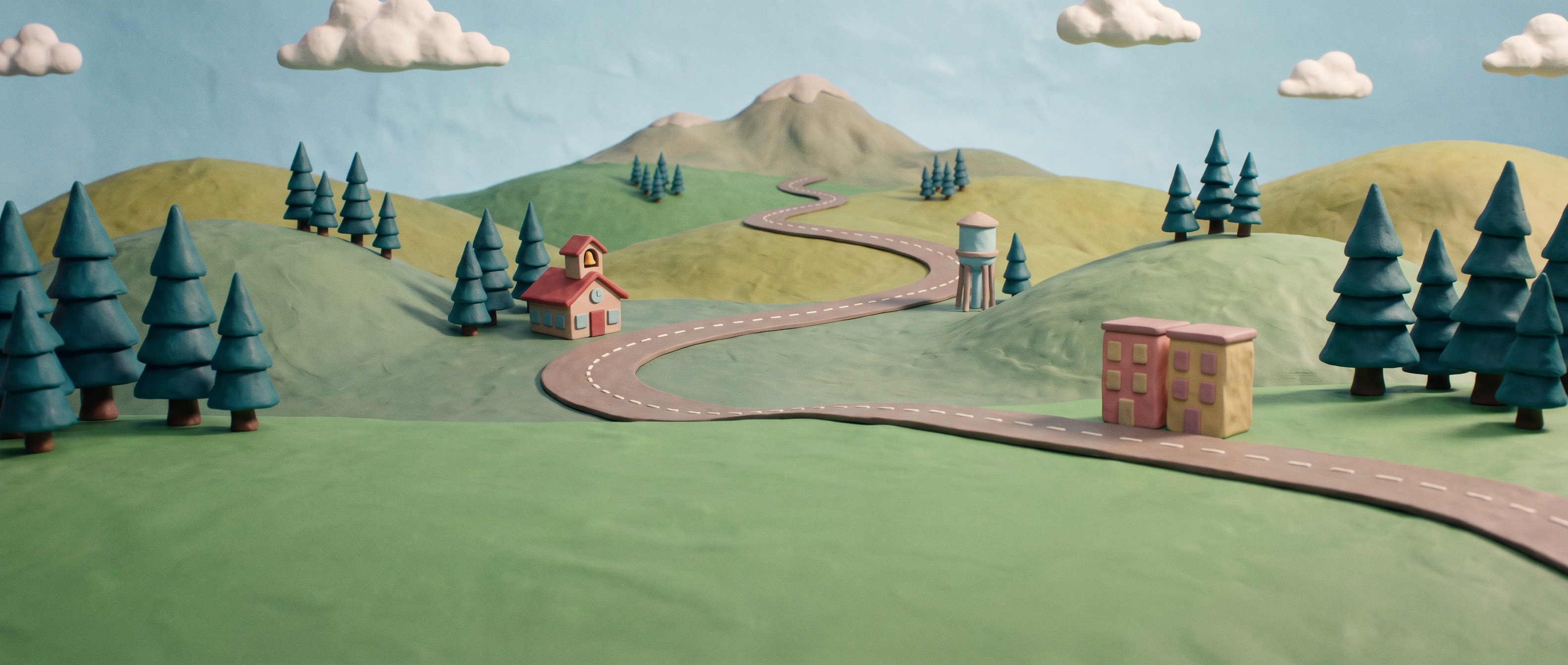A clay road winding over green hills toward a distant mountain, past a small school, a water tower and an apartment block.