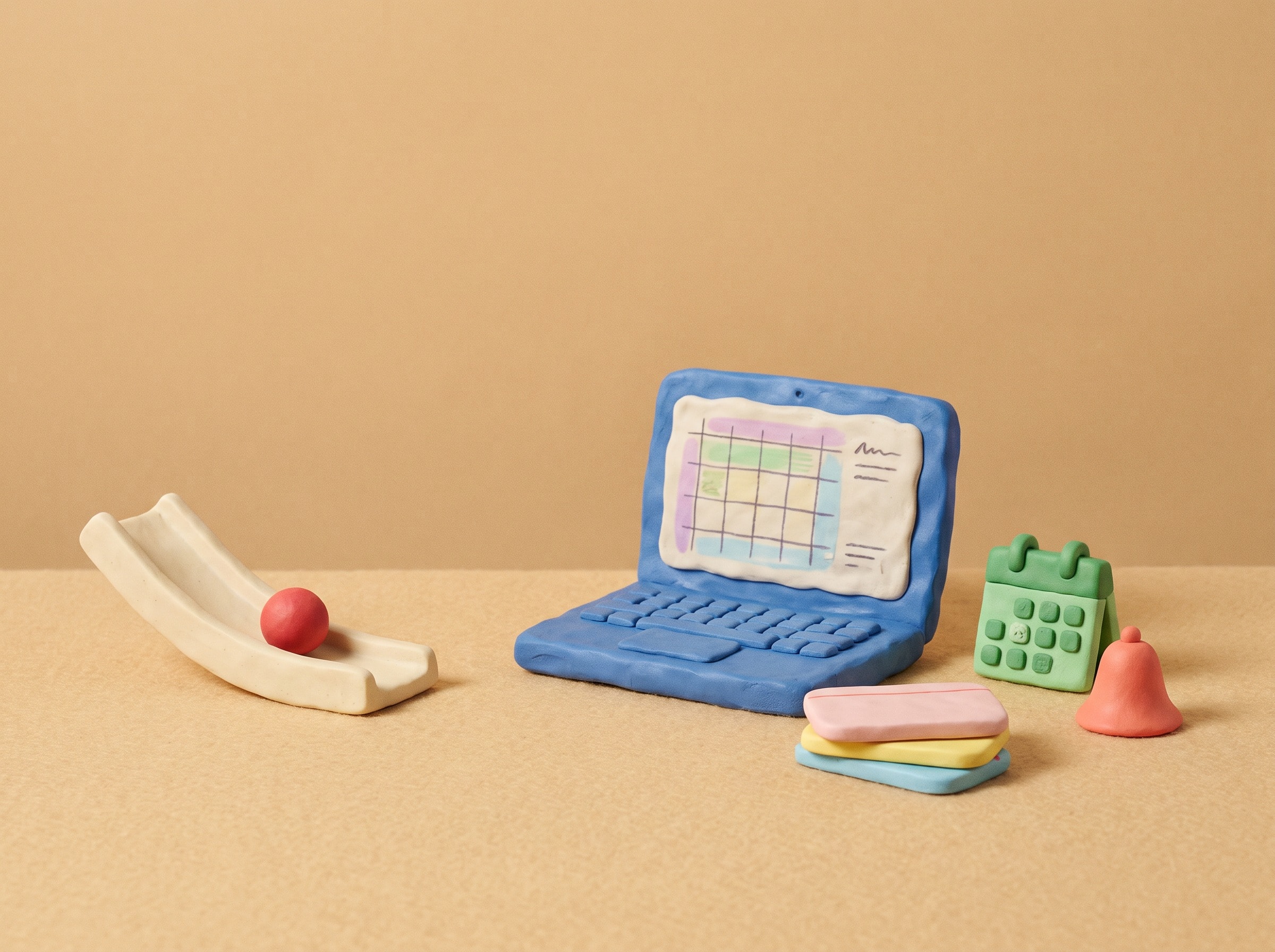 Clay laptop with a spreadsheet, index cards and a small bell on a beige floor.